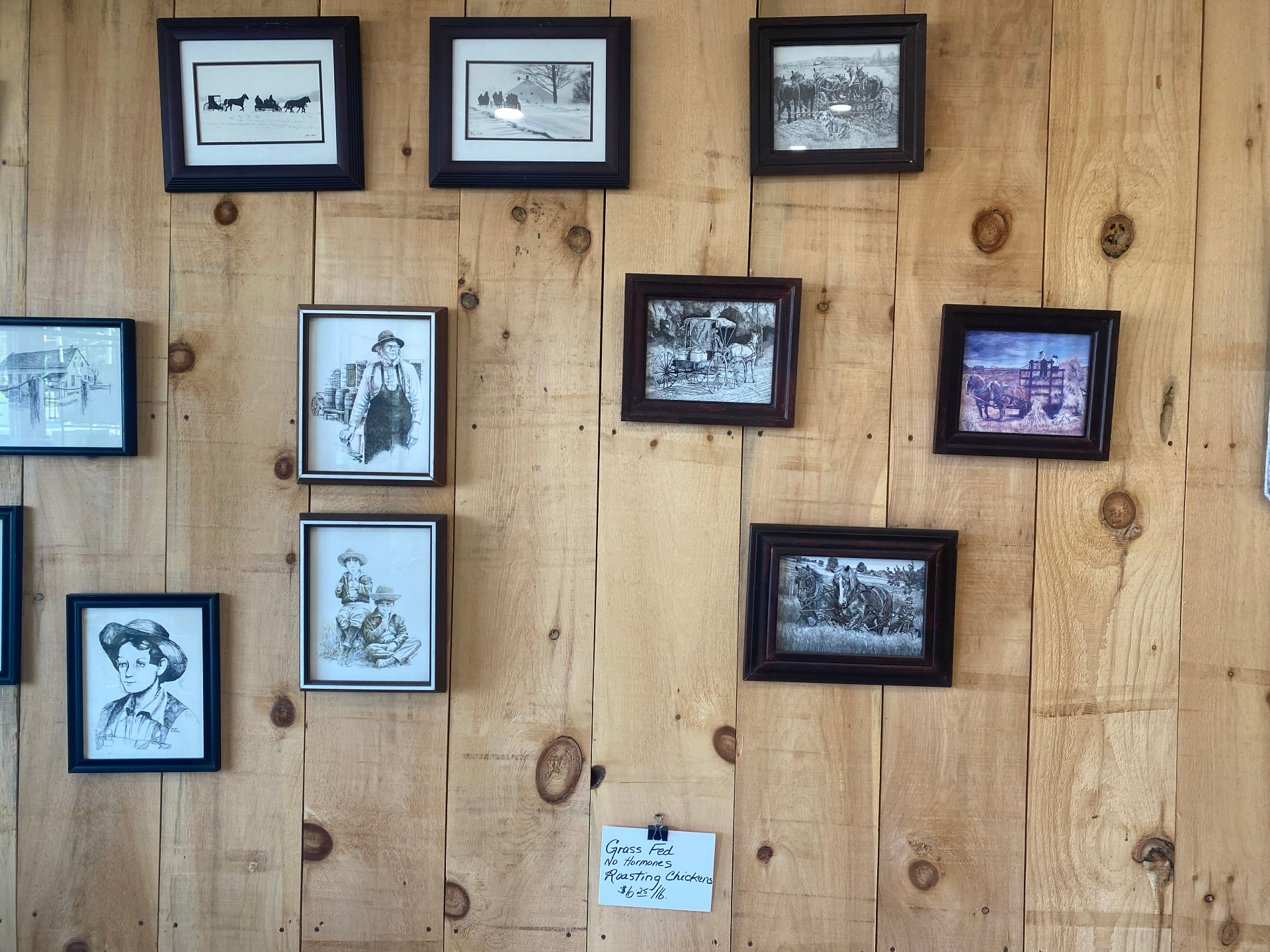 Gallery wall of framed Mennonite and rural heritage artwork inside the market